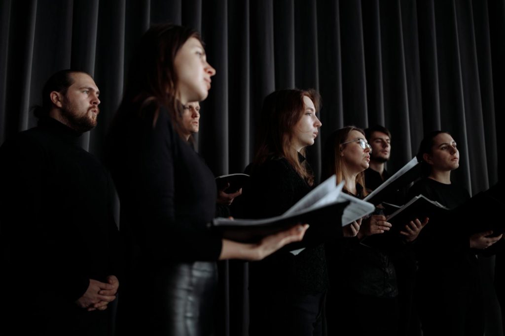 Choir singers in black clothing performing with music sheets indoors, captured from a low angle.